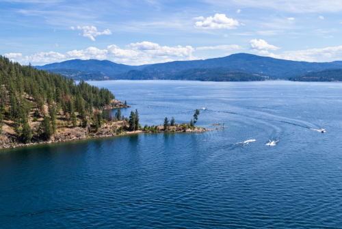 Aerial view of boats on Lake Coeur d'Alene near Tubbs Hill, North Idaho, with surrounding mountains and blue skies.